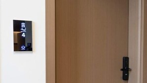 Una puerta de madera con un candado negro y una pantalla digital en la pared a la izquierda.