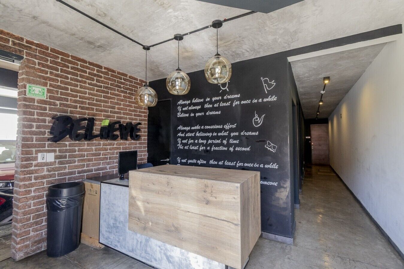 A reception desk with a wooden counter, hanging spherical light fixtures, and a black wall with motivational quotes.