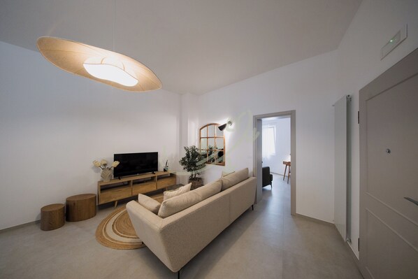 A modern living room with a sofa, TV, wooden sideboard, and a large pendant light. - TD Amalfitana 11 Bell Tower View (Monopoli)