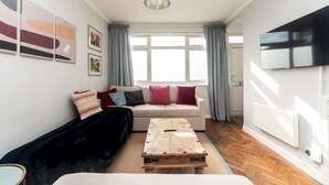 A modern living room with a sofa, a coffee table, and a TV mounted on the wall. - Fulham 2BR Flat | Clean, Quiet & Spacious - Pass the Keys (London)