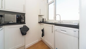 A modern kitchen with white cabinets, a black countertop, a microwave, a dishwasher, and a window with a view. - Fulham 2BR Flat | Clean, Quiet & Spacious - Pass the Keys (London)