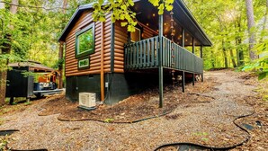 A log cabin with a deck, surrounded by trees. - Luxury Couples Cabin | Hot Tub + Sauna + Theater (Sevierville)