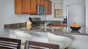 A kitchen with wooden cabinets, a stainless steel refrigerator, a granite countertop, and a bowl of fruit. -  2 Prem. condos in Palm Desert week of 3/1/27 - 1st week of BNP Paribas Tourney (Palm Desert)