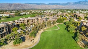 A golf course with a clubhouse, surrounded by residential buildings and mountains in the background. -  2 Prem. condos in Palm Desert week of 3/1/27 - 1st week of BNP Paribas Tourney (Palm Desert)