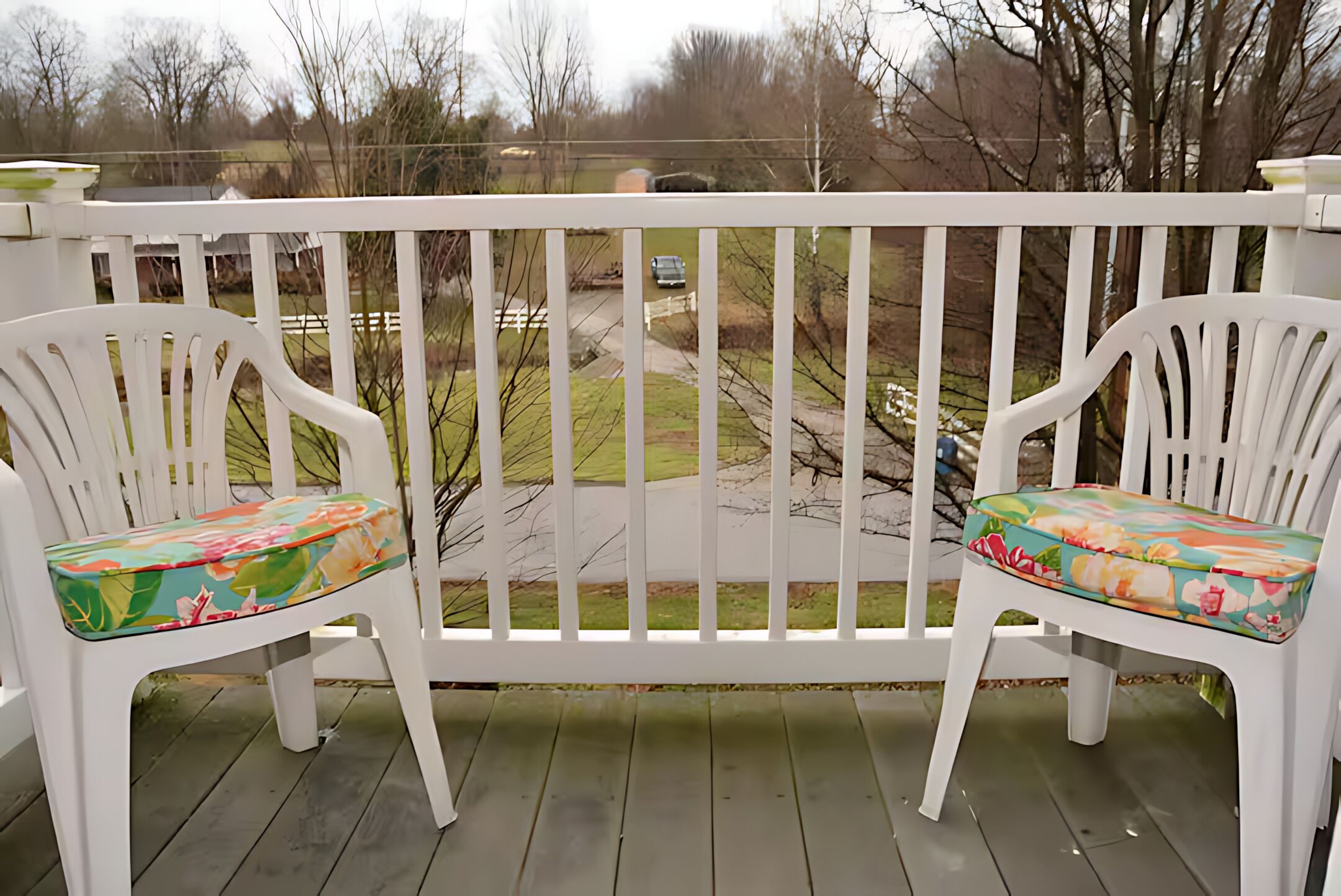 Two white plastic chairs with floral cushions on a wooden deck.