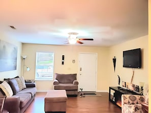 Una sala de estar con ventilador de techo, un sofá, una butaca, un televisor y una chimenea.