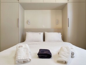 A hotel room with a bed, two pillows, a headboard, and a wall-mounted light fixture. - Hidden Garden Home in Glyfada Center (Glifada)