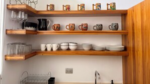 Una cocina con estantes de madera que contienen diferentes vasos, tazas y platos.