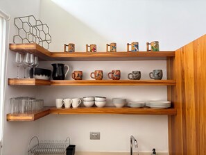 A kitchen with wooden shelves holding various glassware, mugs, and plates. - Bali Style • Villa • Near Whales Tail Beach (Uvita)