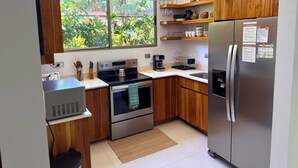 Cocina moderna con armarios de madera, un refrigerador de acero inoxidable y una ventana con vistas a zonas verdes.