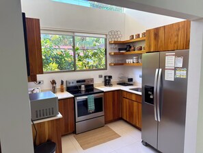A modern kitchen with wooden cabinets, a stainless steel refrigerator, and a window overlooking greenery. - Bali Style • Villa • Near Whales Tail Beach (Uvita)