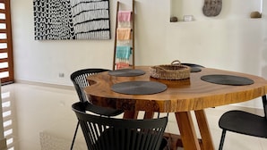 Un comedor con una mesa redonda de madera, sillas negras y individuales tejidas.