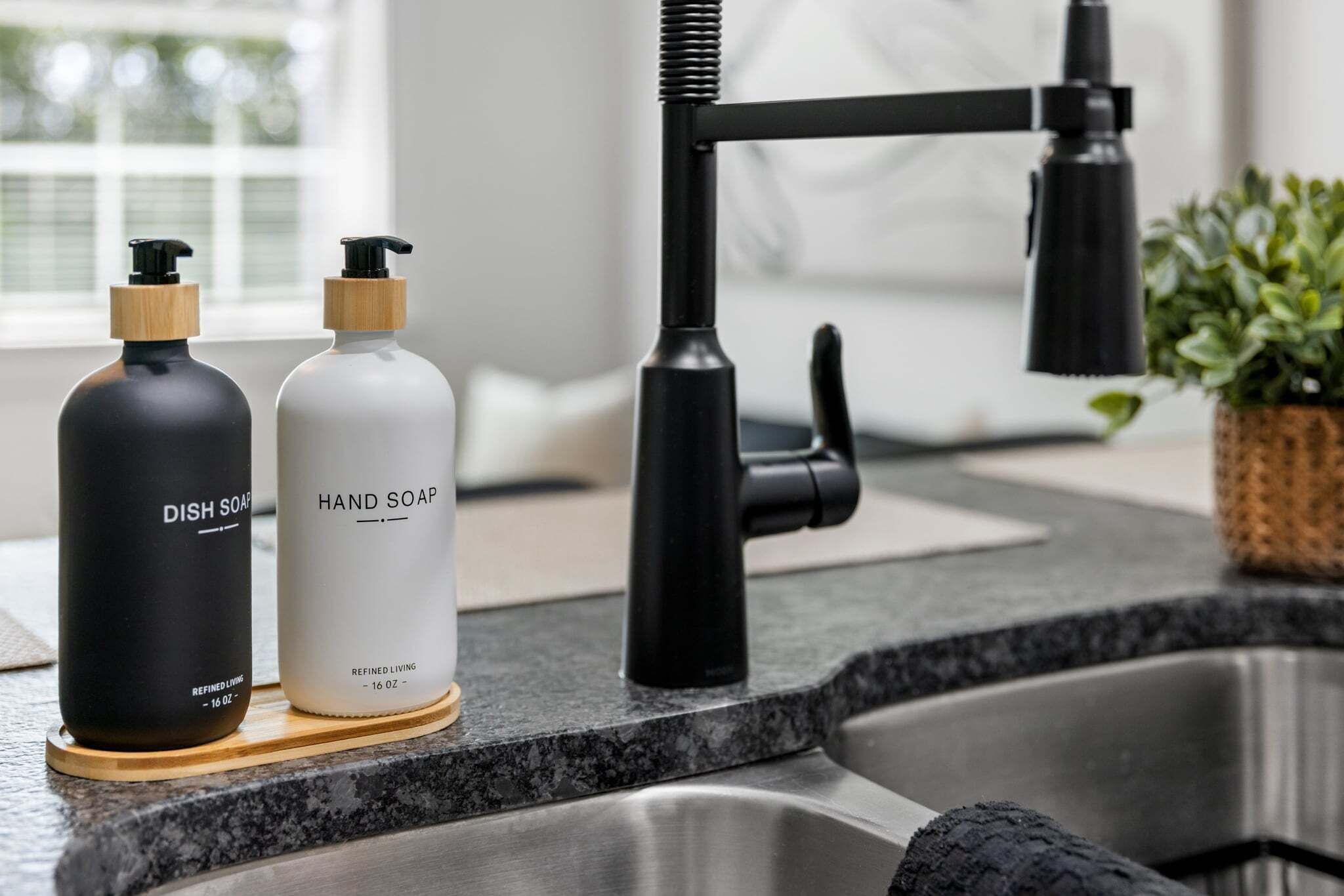 A kitchen with a stainless steel sink, two soap bottles, a black faucet, and a potted plant.
