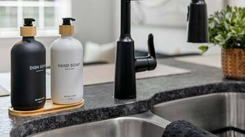A kitchen with a stainless steel sink, two soap bottles, a black faucet, and a potted plant.