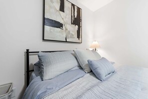 Un llit ben fet amb capçalera, una taula de nit amb una làmpada i un quadre abstracte gran a la paret.