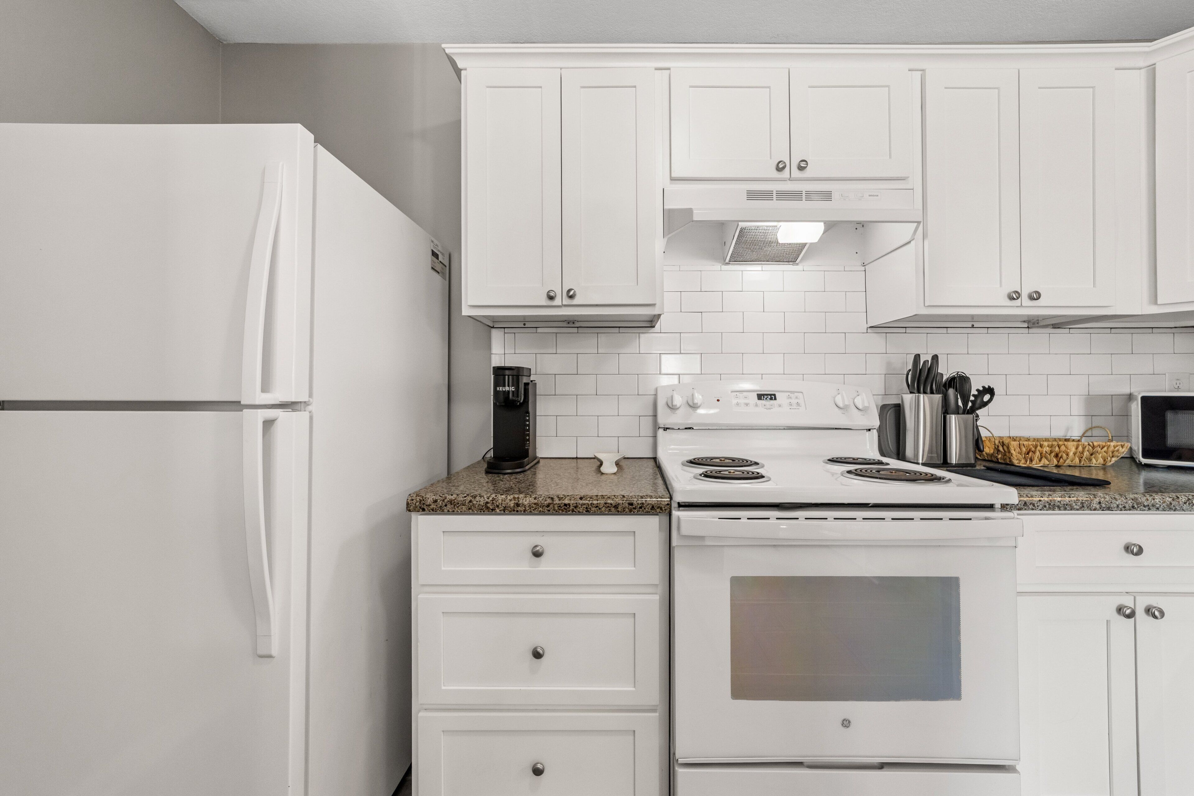 A kitchen with white cabinets, a white refrigerator, a stove, and a microwave.