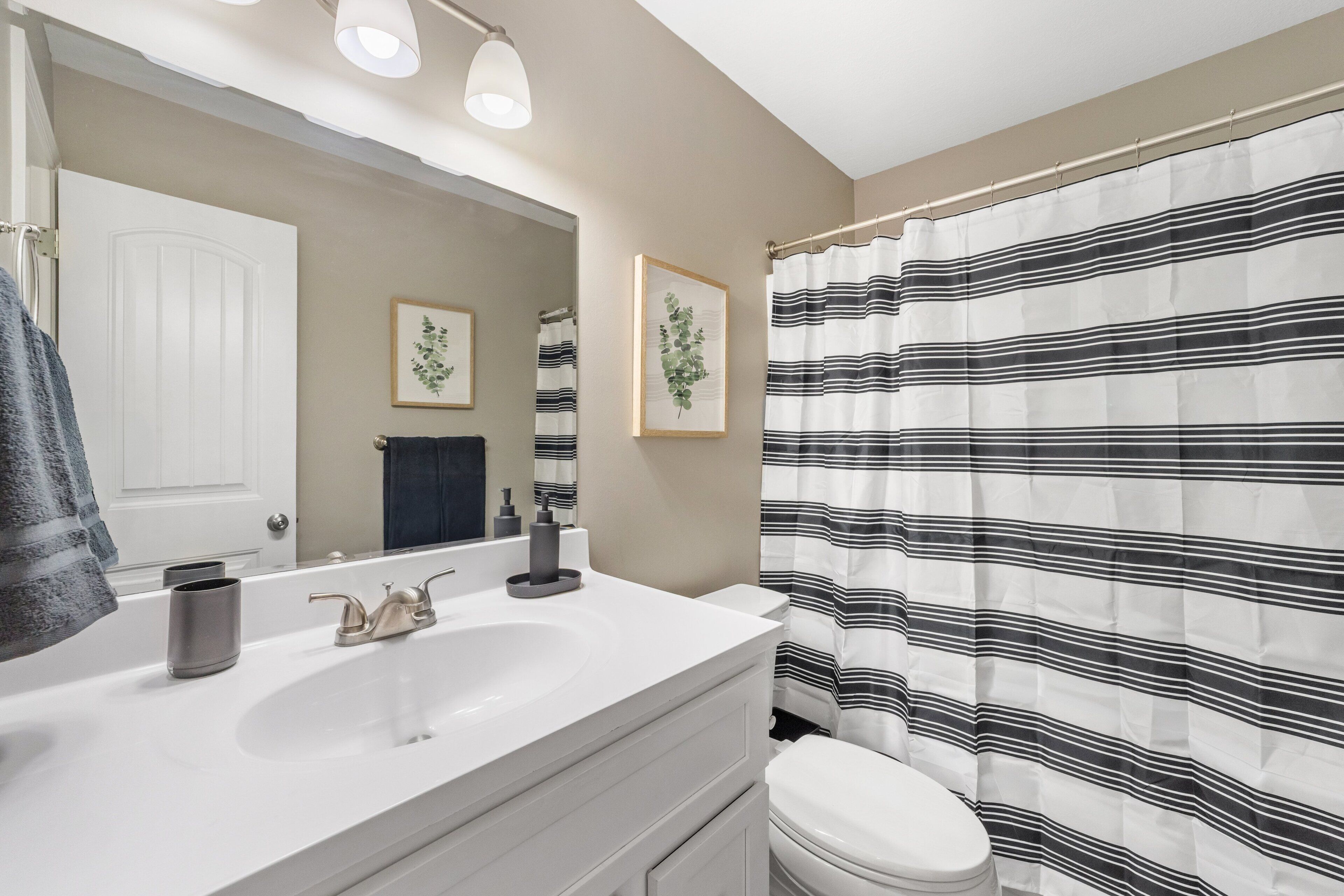A bathroom with a white sink, a mirror, a toilet, and a striped shower curtain.