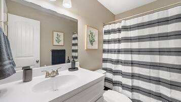 A bathroom with a white sink, a mirror, a toilet, and a striped shower curtain.