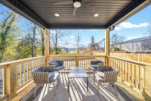 An outdoor deck with a table and chairs, a wooden railing, and a view of trees and houses. - Main Street Manor - Spacious Home Near Dining (Clarksville)