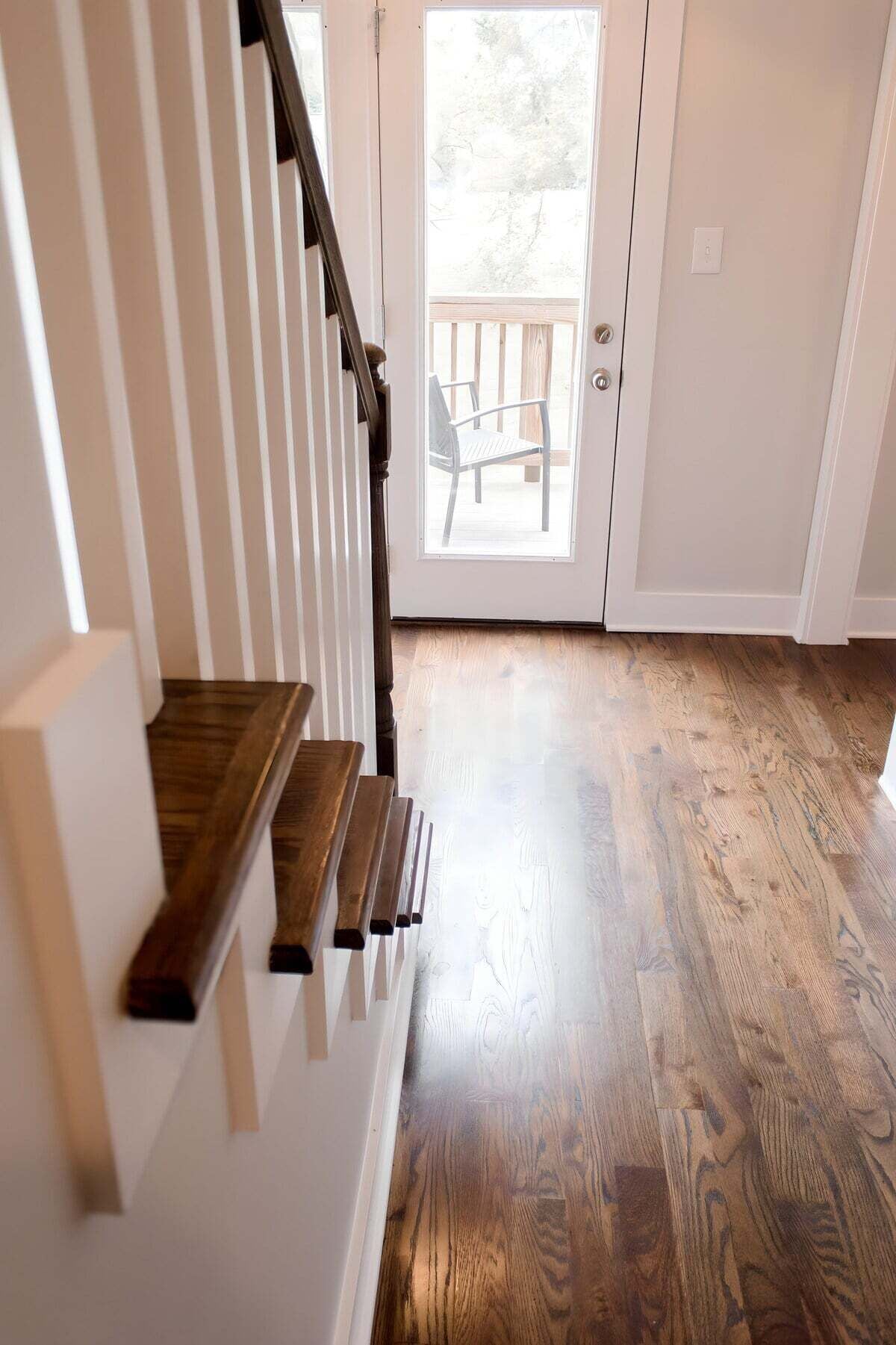 A staircase with wooden steps leading to a door, a wooden floor, and a view of an outdoor deck through a glass door.