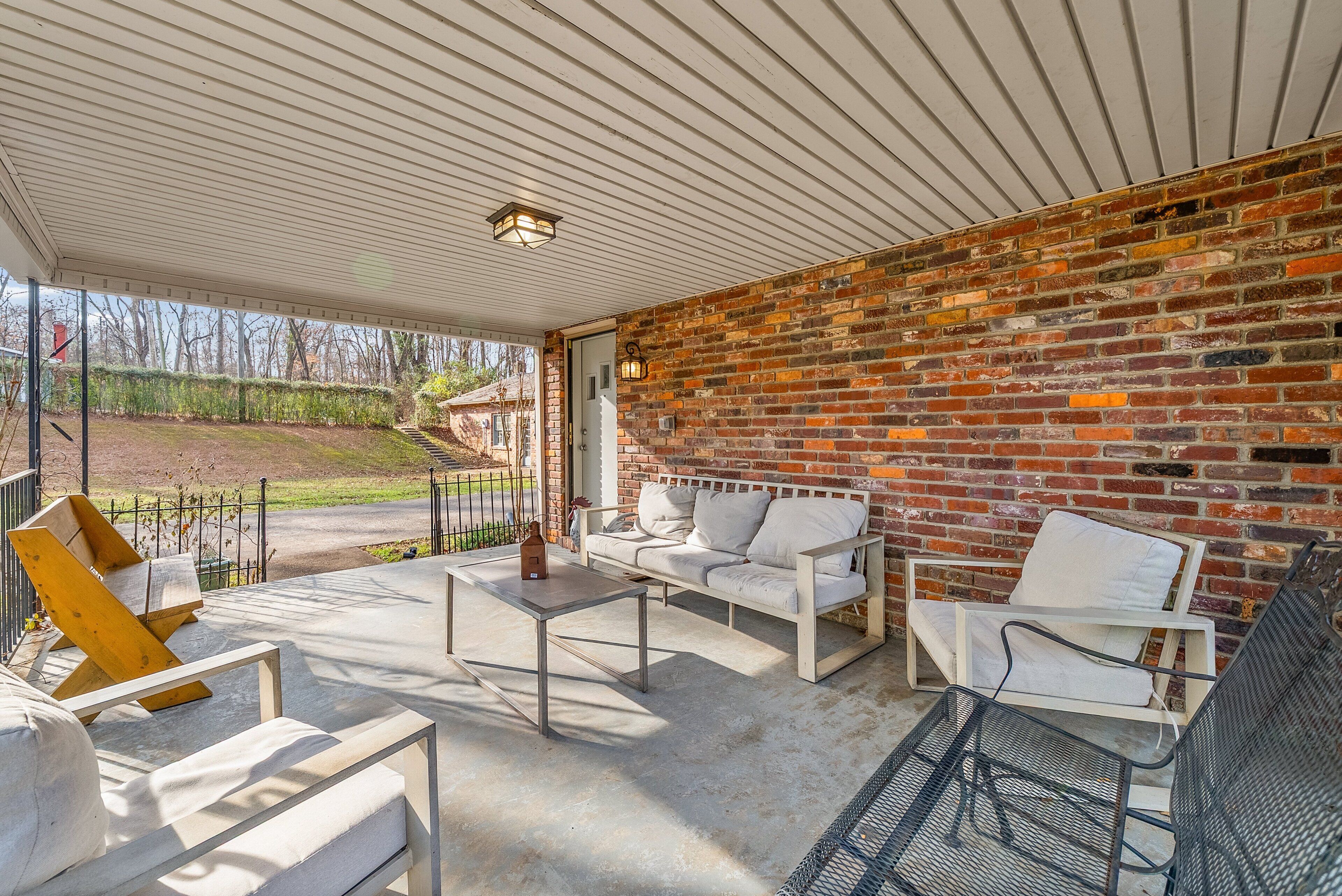 Une terrasse couverte avec un mur en briques, des meubles blancs et une chaise en métal.