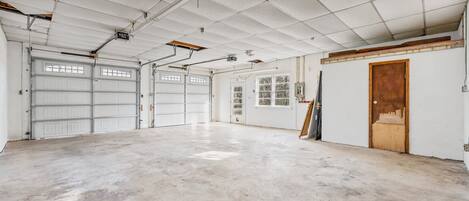 A spacious garage with two large white garage doors, a concrete floor, and a wooden door on the right.