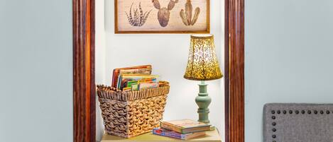 Une table de chevet avec un panier en osier, des livres, une lampe et un tableau encadré accroché au mur.