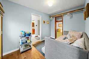 Ett sovrum med en grå soffa, en byrå i trä och en hall som leder till ett badrum.