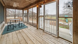 Un porche cubierto con mesa y bancos, ventanas amplias y vistas al exterior.