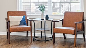 Two brown leather chairs with a white and blue pillow, a small round table with a vase and mug, and a window with blinds. - Cottage With Community Pool (Clarksville)