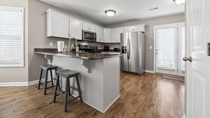 A modern kitchen with white cabinetry, a stainless steel refrigerator, a microwave, and a granite countertop island with two stools. - Cottage With Community Pool (Clarksville)