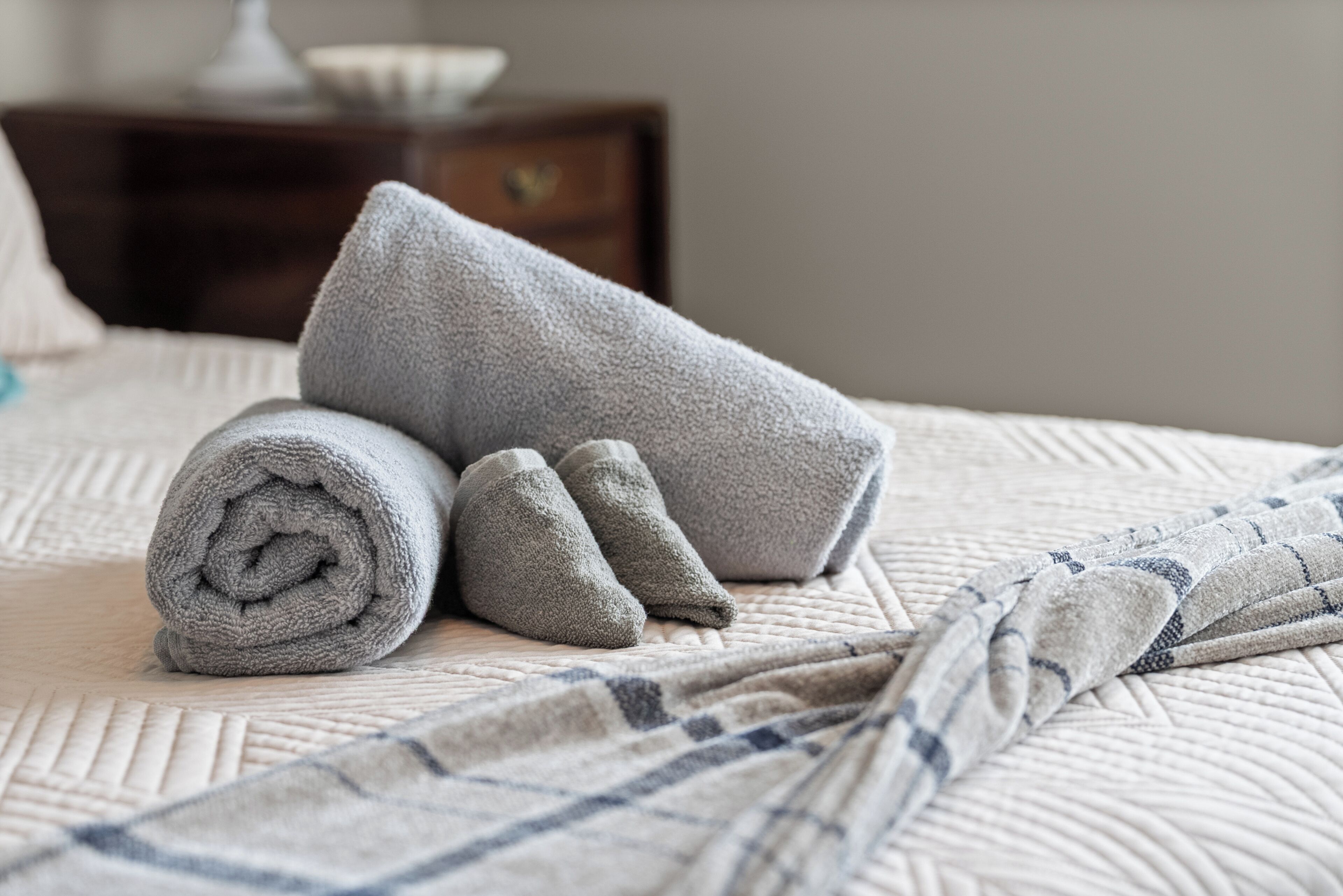 A neatly made bed with rolled towels and a checkered blanket.