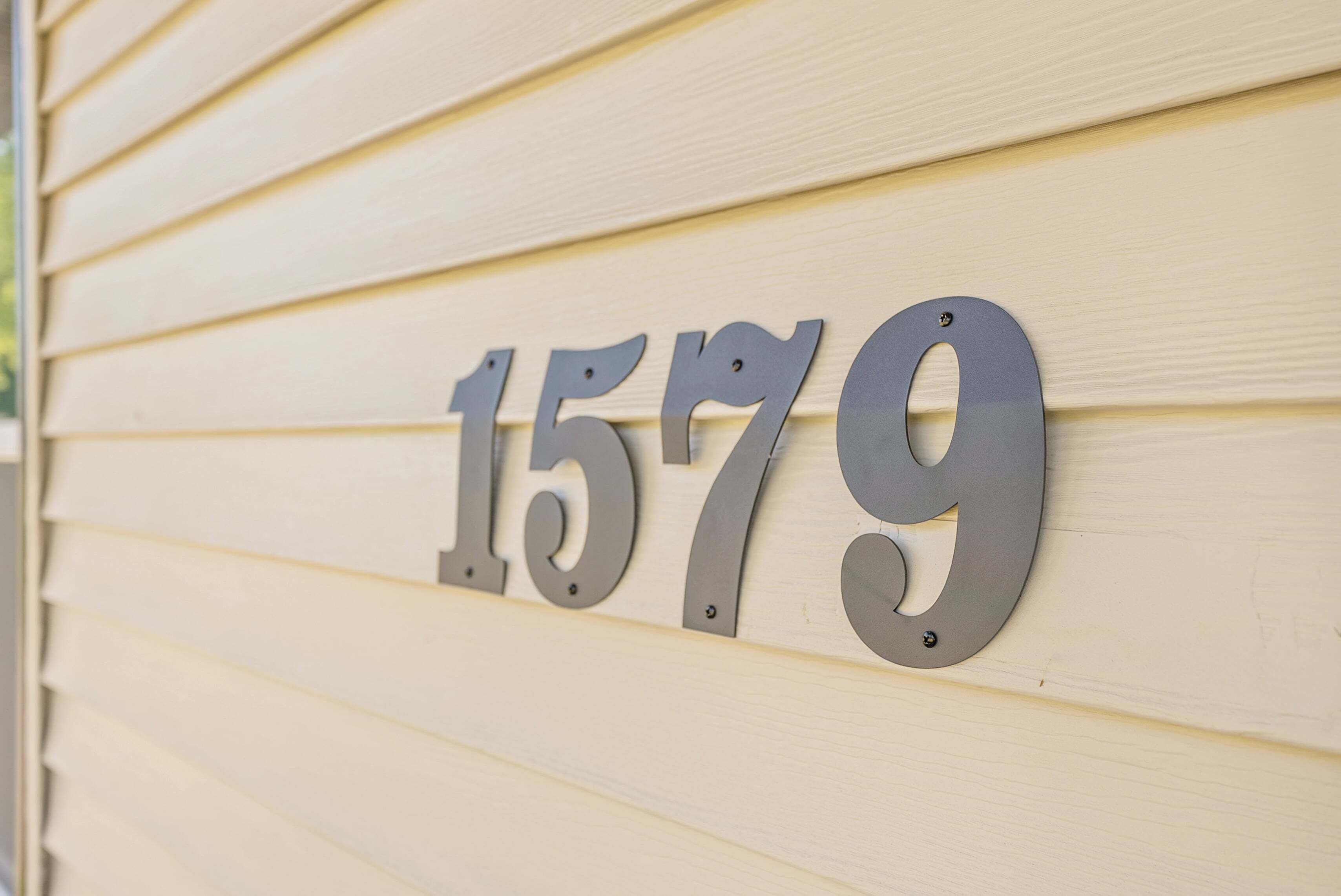Une plaque en métal indiquant le numéro de la maison, fixée sur un mur recouvert de bardage beige.
