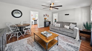 A living room with a sofa, coffee table, dining table with chairs, a ceiling fan, and a clock on the wall. - Enjoy Our 936sf Single-story Home With a Private Entrance (Clarksville)