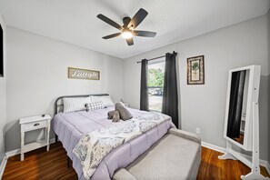 A bedroom with a bed, a nightstand, a ceiling fan, a window with curtains, and a framed picture on the wall. - Enjoy Our 936sf Single-story Home With a Private Entrance (Clarksville)