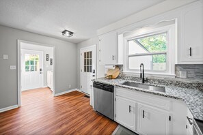A kitchen with white cabinets, a granite countertop, a dishwasher, and a window with a view of greenery. - Enjoy Our 936sf Single-story Home With a Private Entrance (Clarksville)