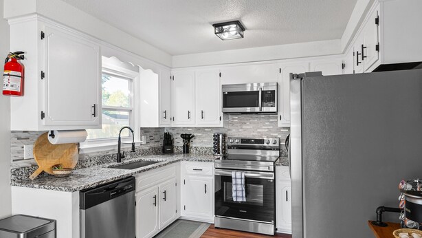 A modern kitchen with white cabinets, stainless steel appliances, a fire extinguisher, and a wooden cutting board. - Enjoy Our 936sf Single-story Home With a Private Entrance (Clarksville)