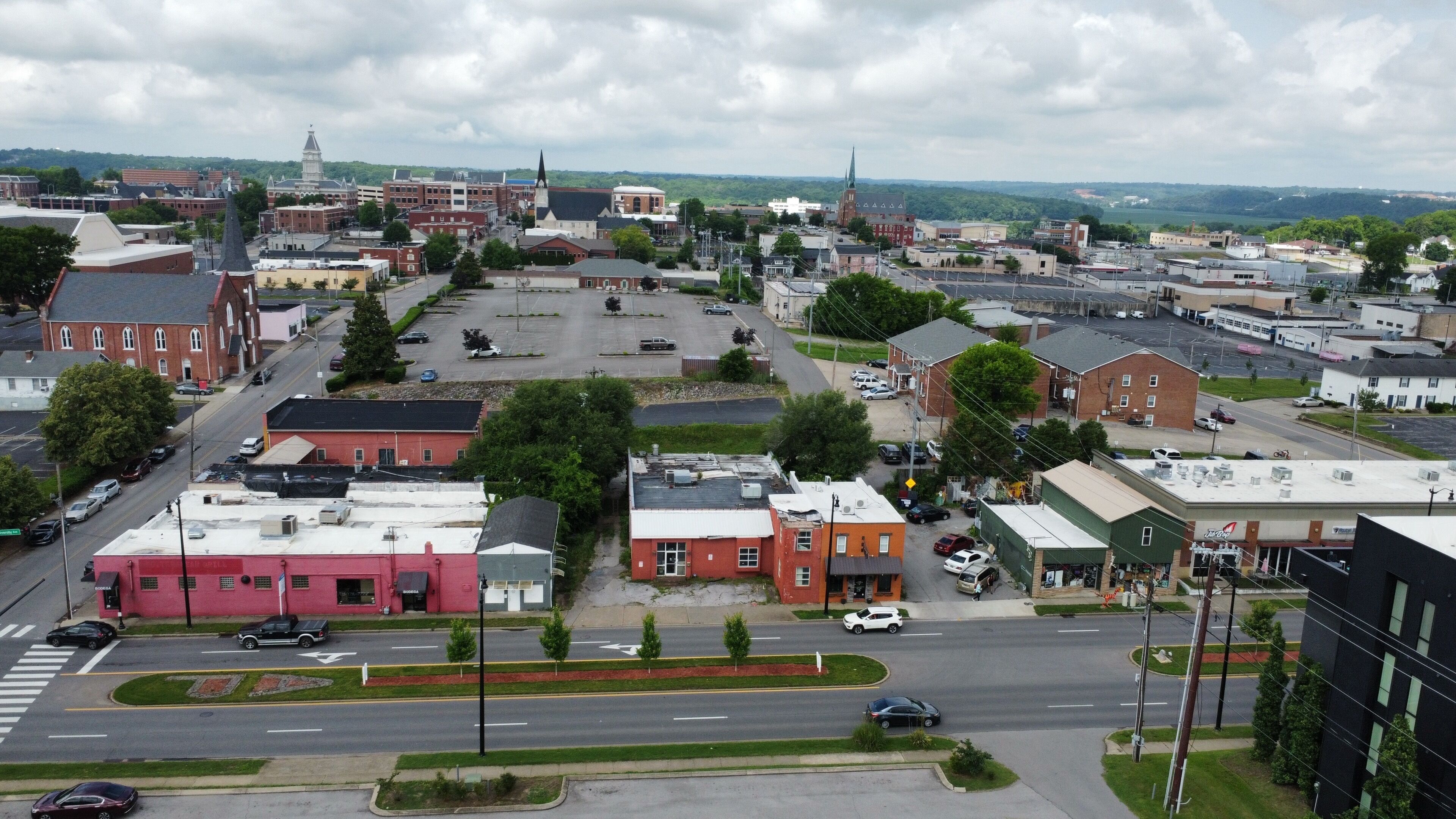 A town with a mix of commercial and residential buildings, a prominent church steeple, and a large parking lot.