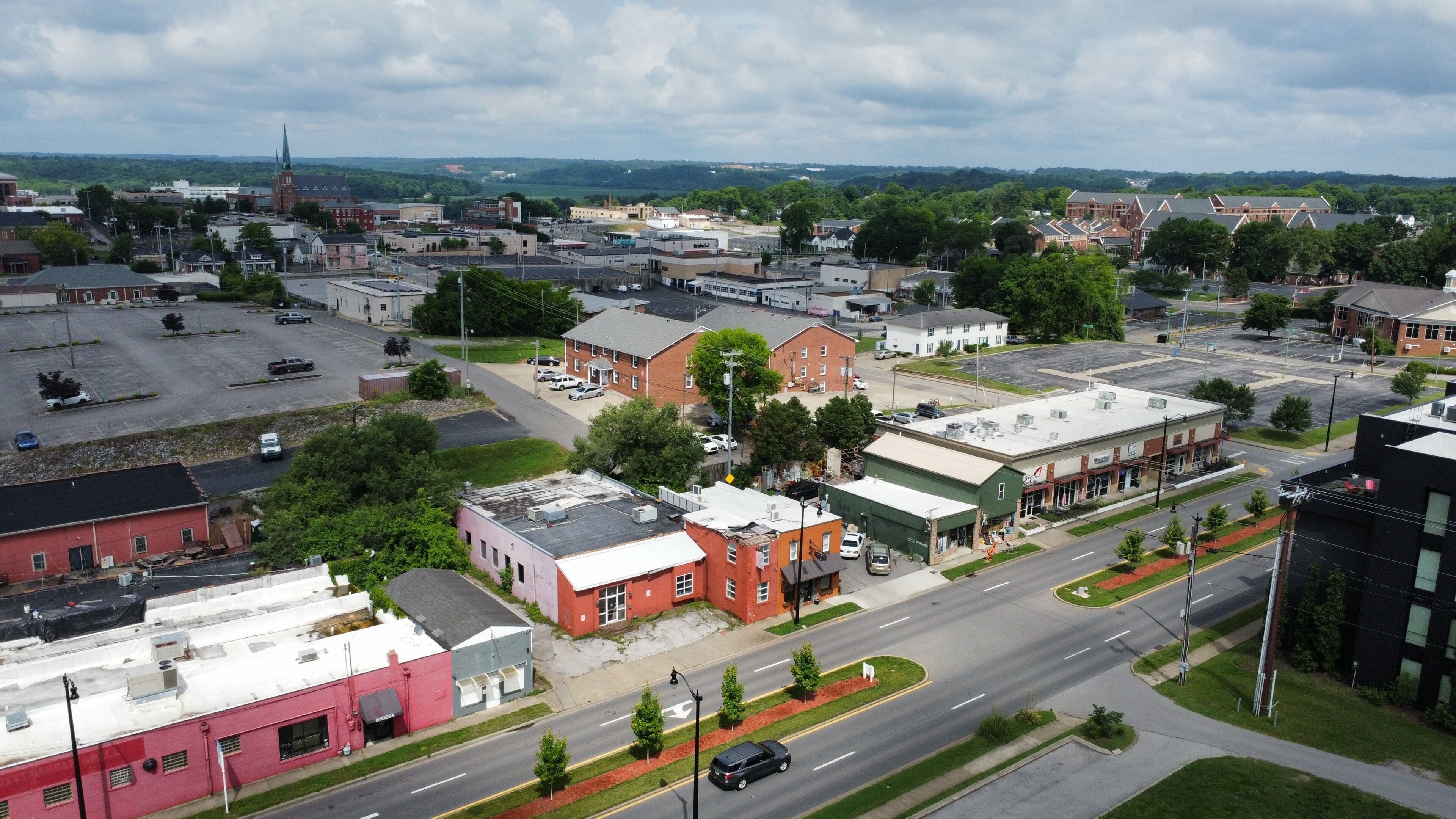 Une ville où se côtoient des bâtiments commerciaux et des immeubles d’habitation, une rue principale et un parking.