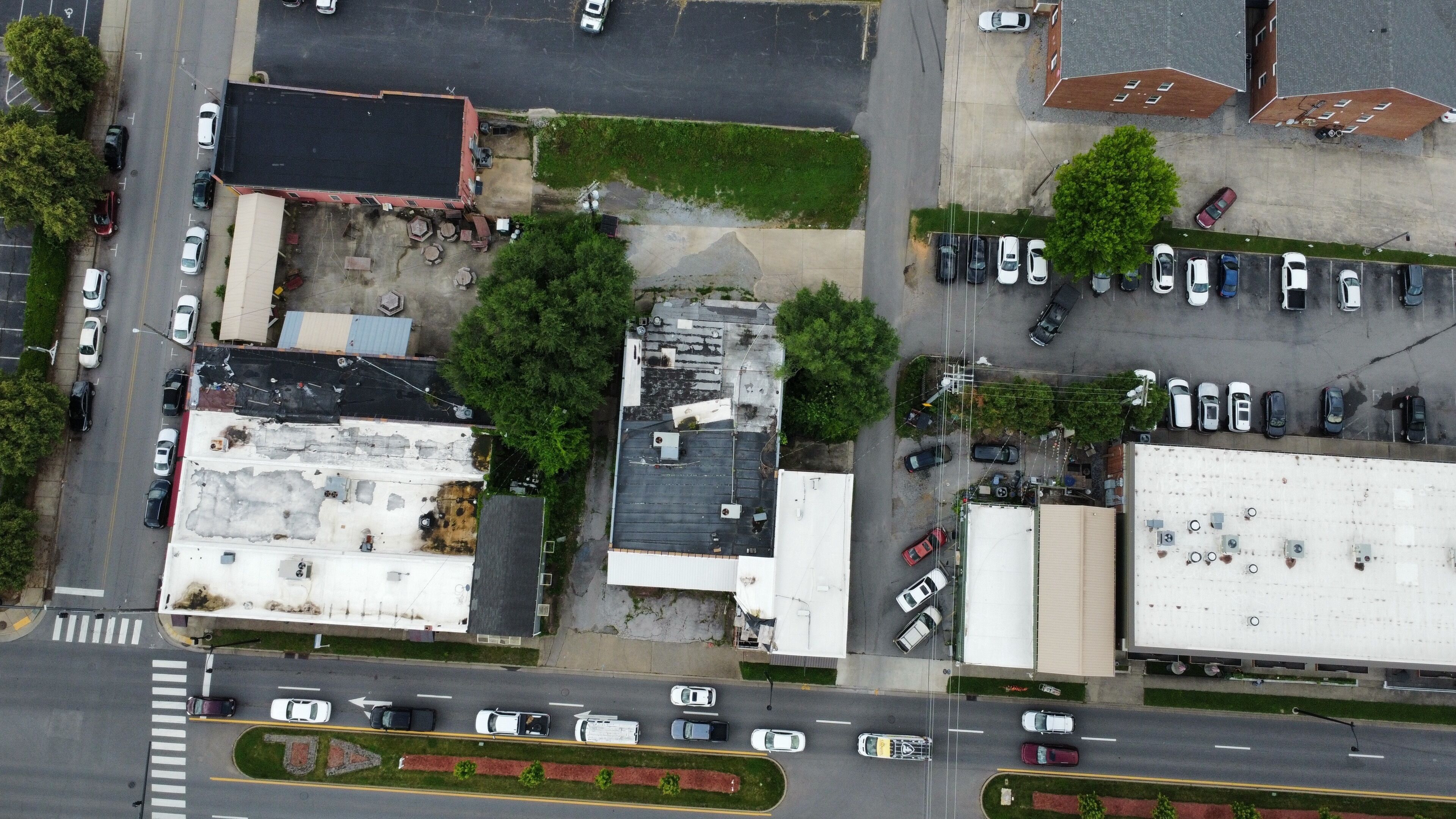 An aerial view of a parking lot with multiple cars, a building with a flat roof, and a road with traffic.