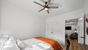 Une chambre à coucher avec un lit, un ventilateur de plafond et une vue sur le salon.