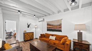 Un salon comprenant un canapé, une table basse, une lampe, une tête de cerf fixée au mur et une fenêtre avec des rideaux.
