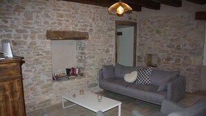 Una habitación con paredes de piedra, un sofá gris, una mesa de centro blanca y un mueble de madera.