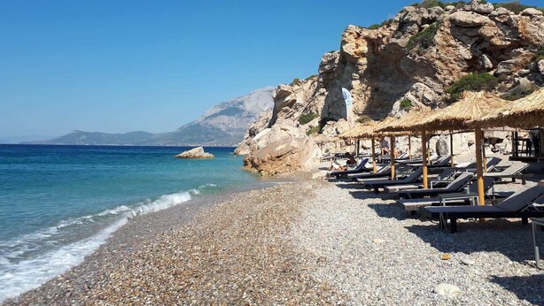 Une plage de galets avec des chaises longues et une structure surmontée d’un toit de chaume.