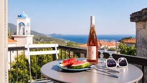 Une table avec une bouteille, des verres et une pastèque, placée sur un balcon donnant sur un paysage magnifique.