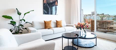 A modern living room with a sofa, a coffee table, and a large window with a city view.