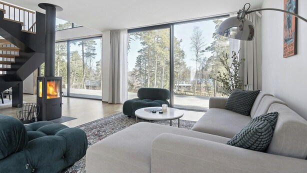 A modern living room with a fireplace, large windows, a staircase, and a sofa. - Airy house with large glass fronts on Adelsö (Adelsö)
