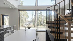 A modern kitchen with a dining area, large windows, and a wooden staircase. - Airy house with large glass fronts on Adelsö (Adelsö)