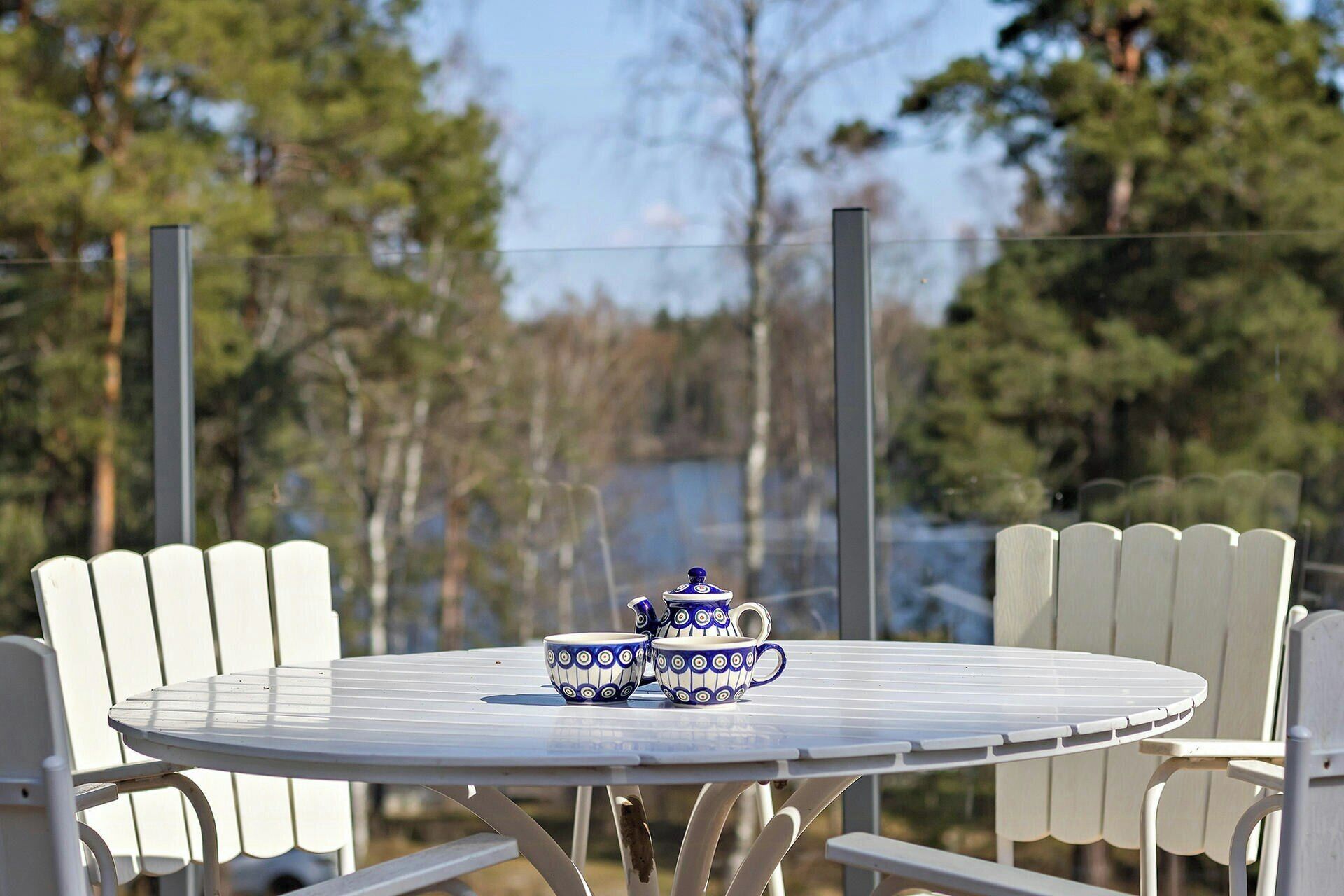A round metal table with a white chair arrangement, a blue and white patterned pitcher, and a cup on the table.