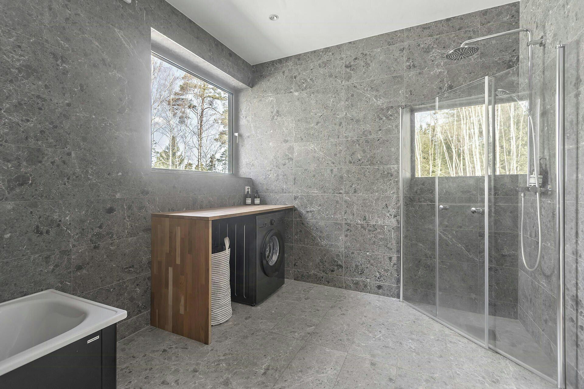 Une salle de bain moderne avec une douche à parois de verre, un meuble-lavabo en bois, un lave-linge et une grande fenêtre.